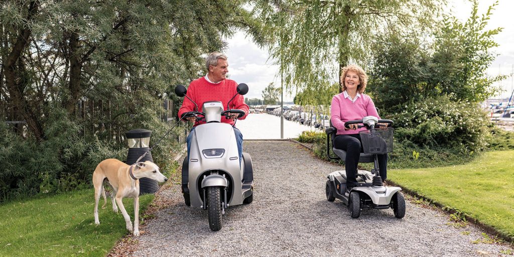Man och kvinna på varsin promenadscooter. Kör på grusväg vid en båthamn.